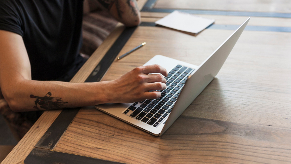  close up de homem com tatuagem no braço usando laptop (Fonte: Freepik)